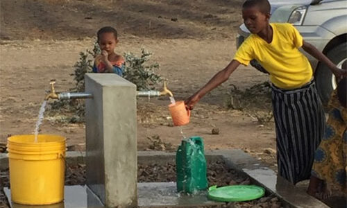 Two children stand at a well filling buckets with water at the Singida Solar Project site.